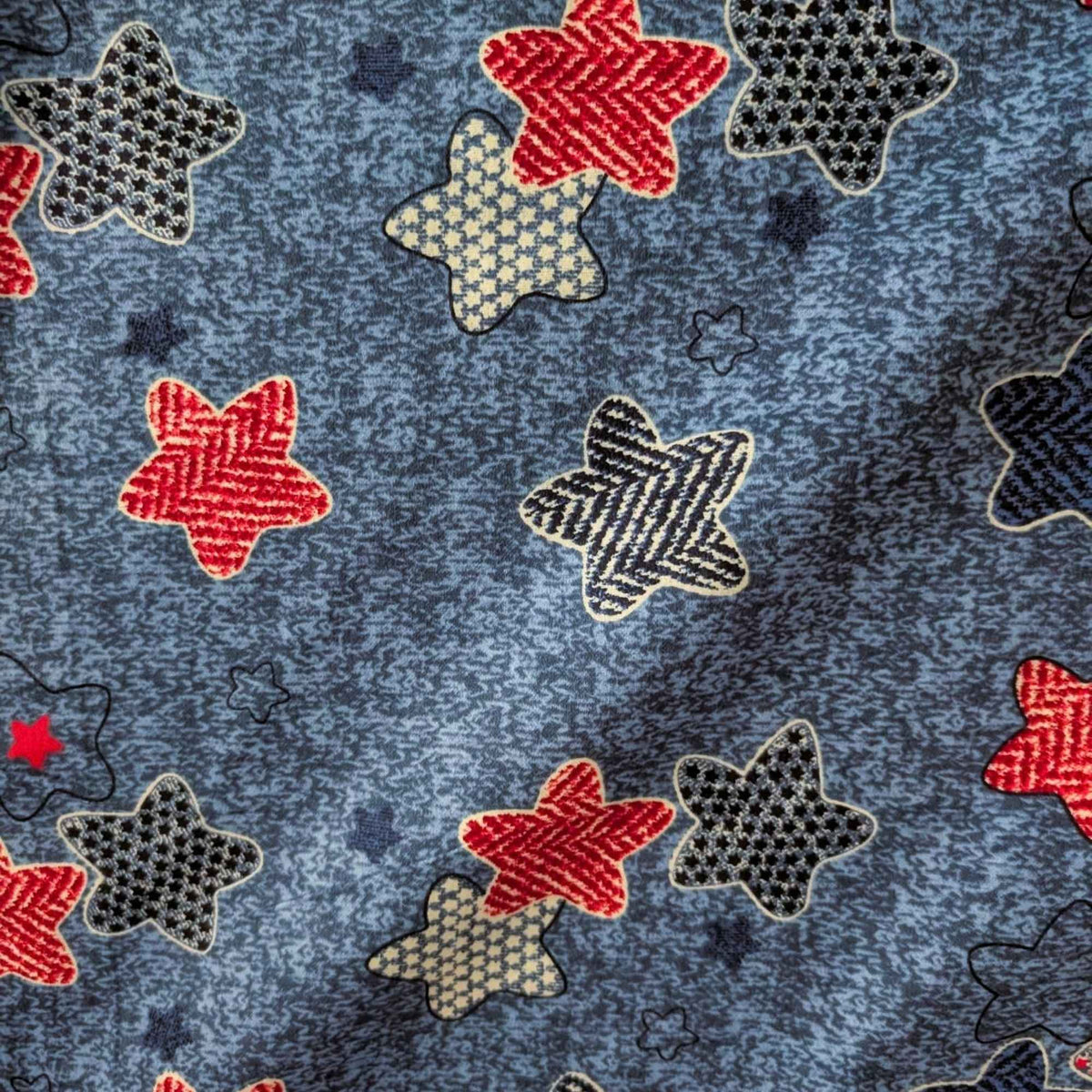 Star print cotton flannel with red, navy, black and cream patterned stars on a textured denim-look blue background.