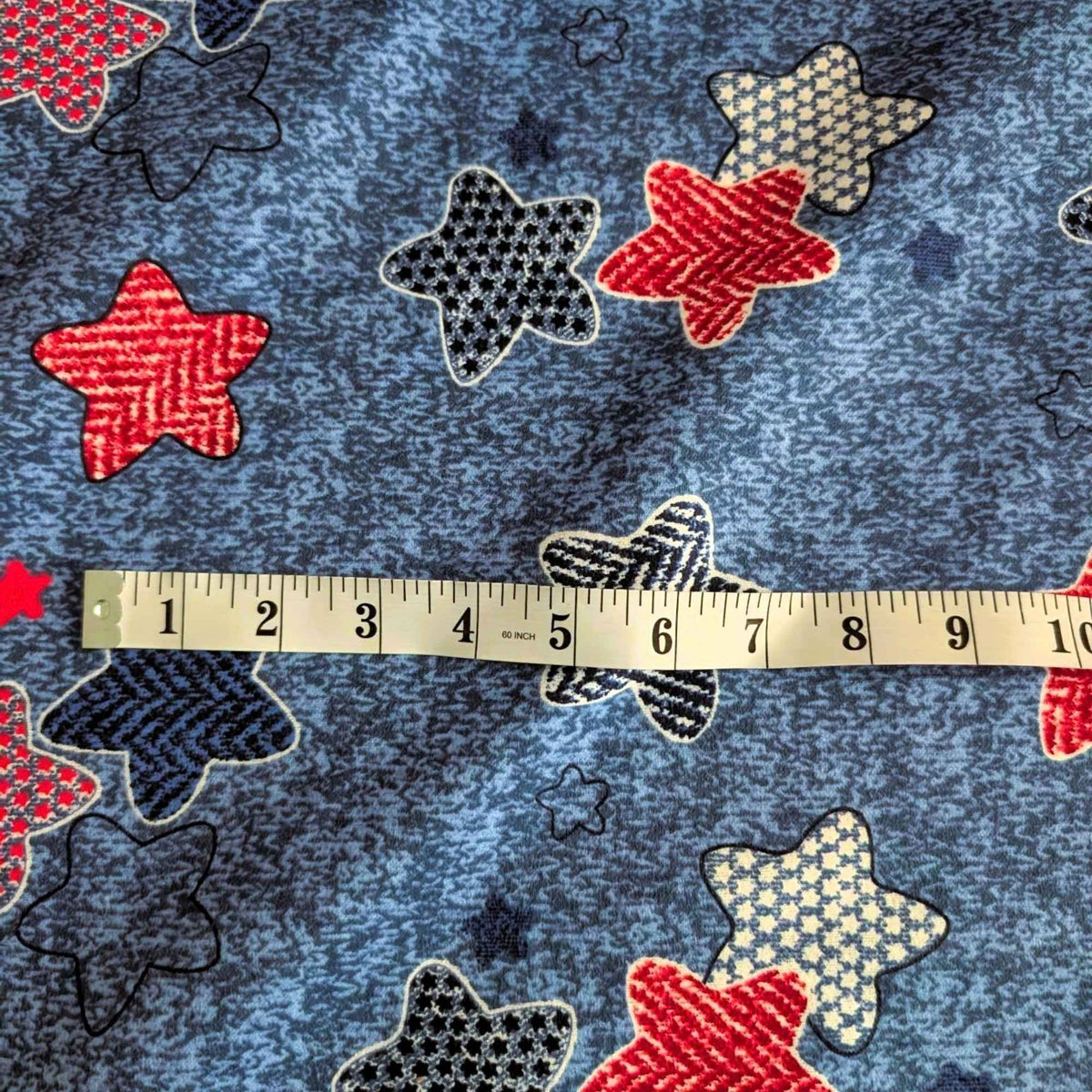 Star print cotton flannel with red, navy, black and cream patterned stars on a textured denim-look blue background.
