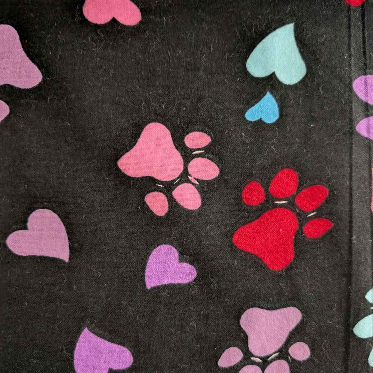 Black cotton flannel fabric with scattered paw prints and hearts in pink, purple, red, turquoise and aqua