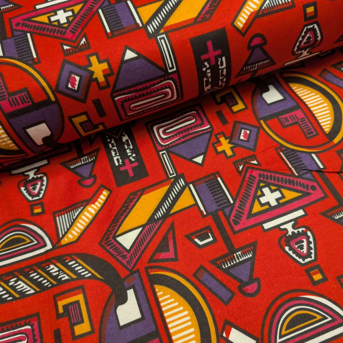 African-inspired geometric tribal double brushed flannel fabric featuring colorful abstract symbols and ethnic geometric patterns on a red background.
