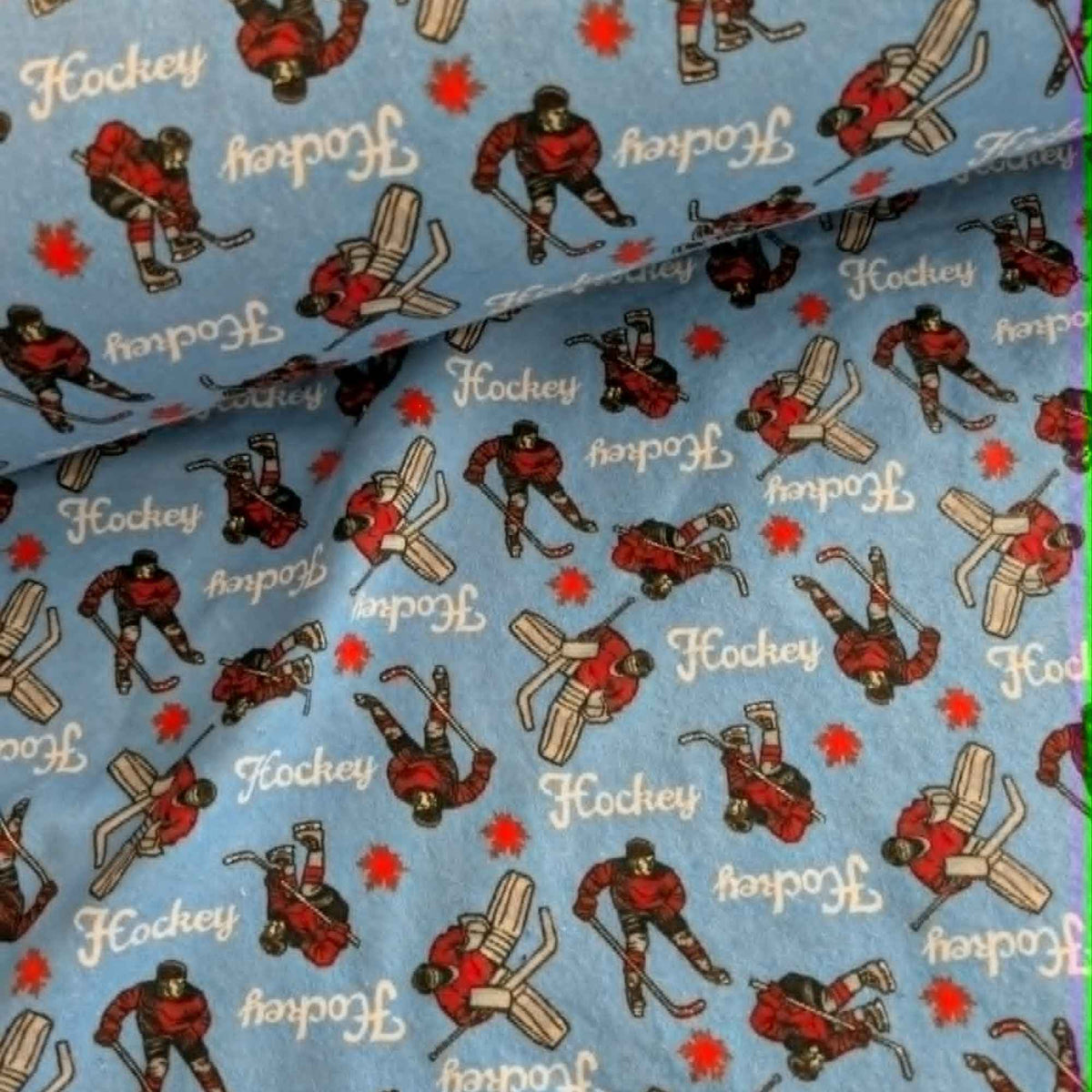 Blue hockey cotton flannel fabric featuring hockey players, goalies, hockey sticks, and hockey text on a soft brushed cotton background.