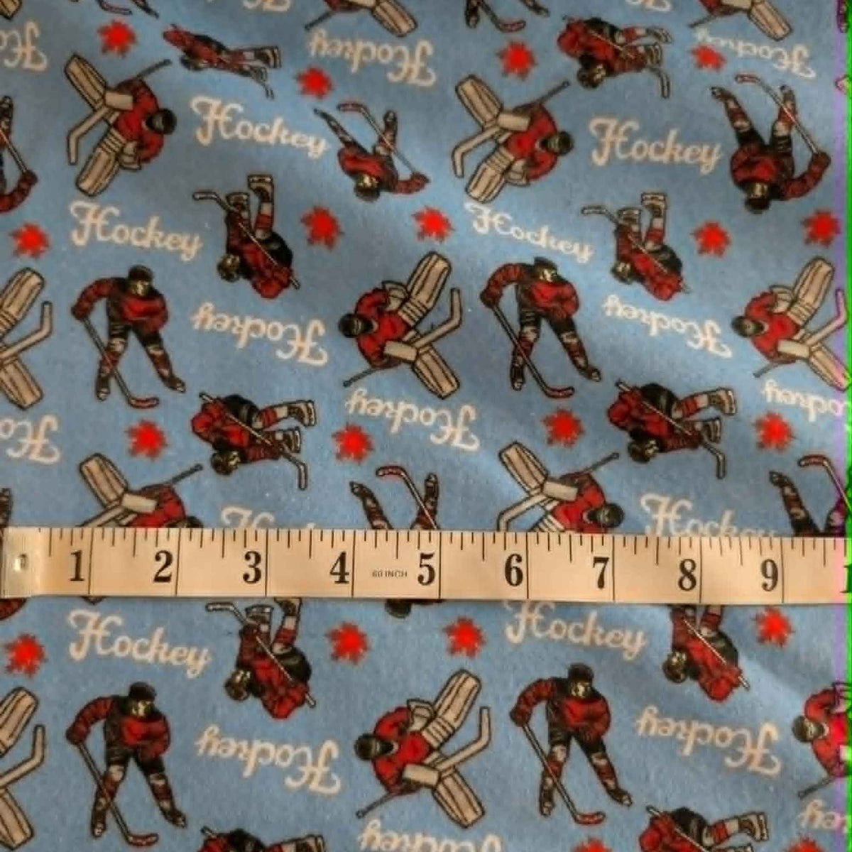 Blue hockey cotton flannel fabric featuring hockey players, goalies, hockey sticks, and hockey text on a soft brushed cotton background.
