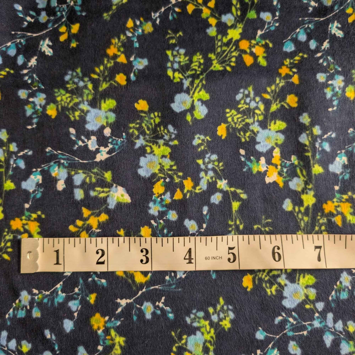 Double brushed flannel fabric featuring delicate yellow, blue, and green wildflowers with trailing vines on a navy background.