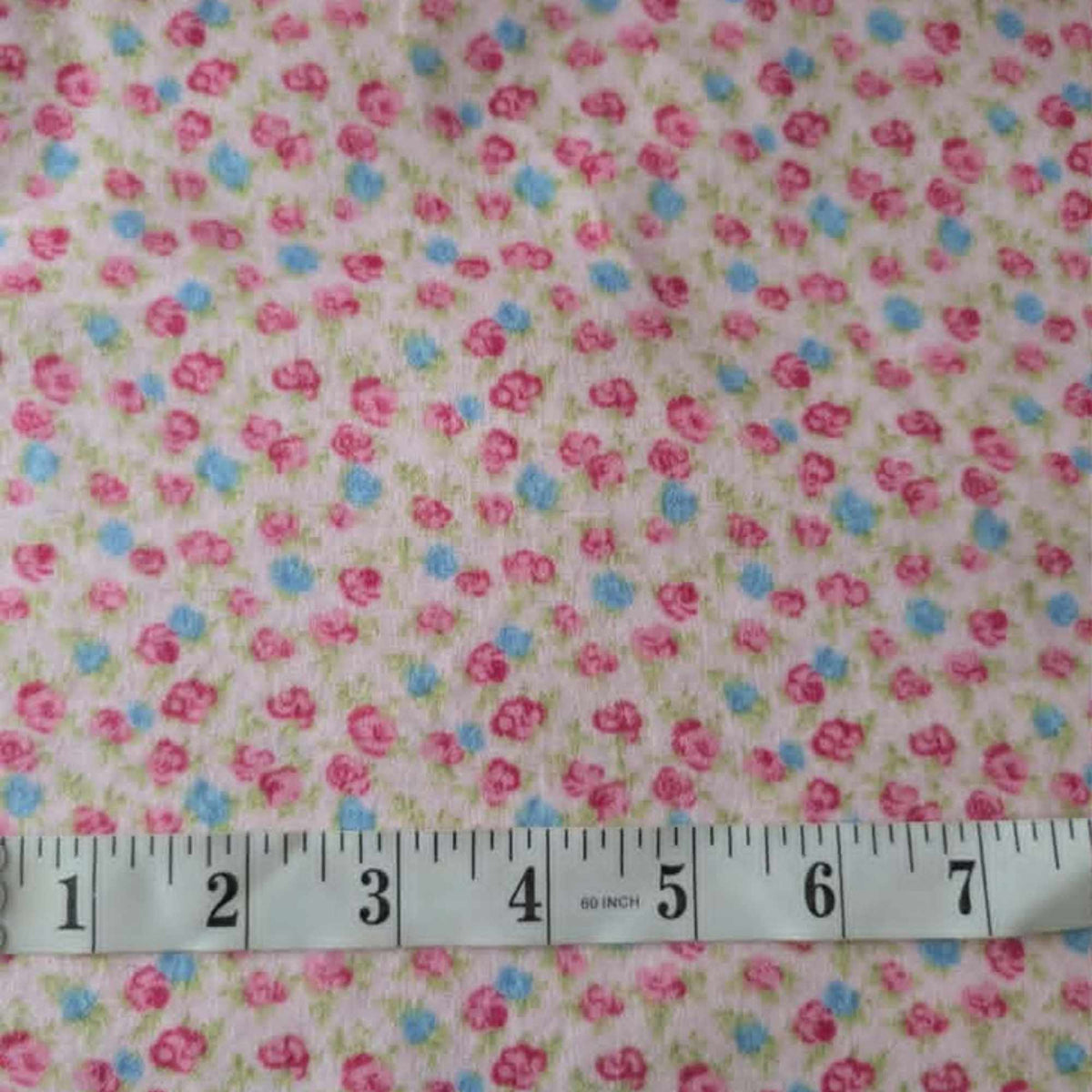 Double brushed flannel fabric featuring tiny pink rosebuds, soft blue flowers, and green foliage scattered across a pink background.