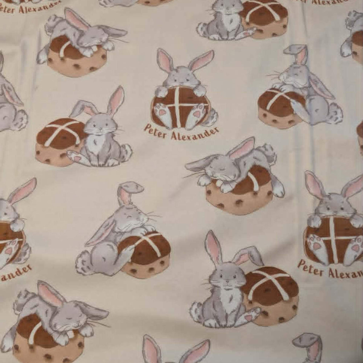 Double brushed flannel fabric featuring adorable bunny rabbits resting beside hot cross buns on a cream background.