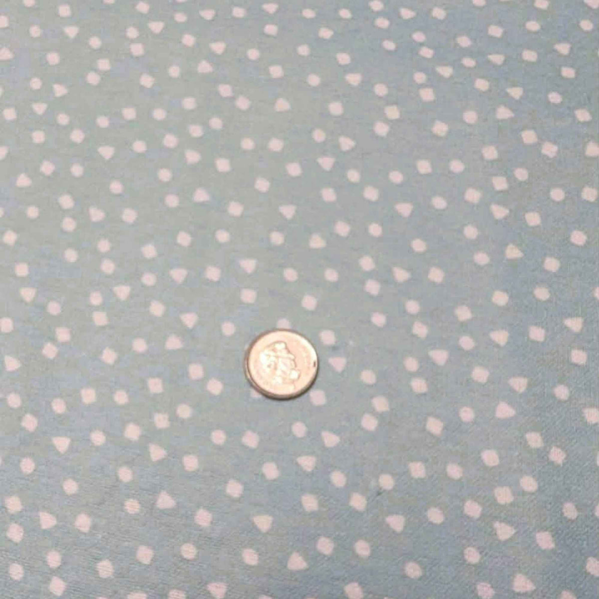 A close-up of a light blue fabric with a repeating pattern of small white hearts, with a small coin placed in the center for scale.