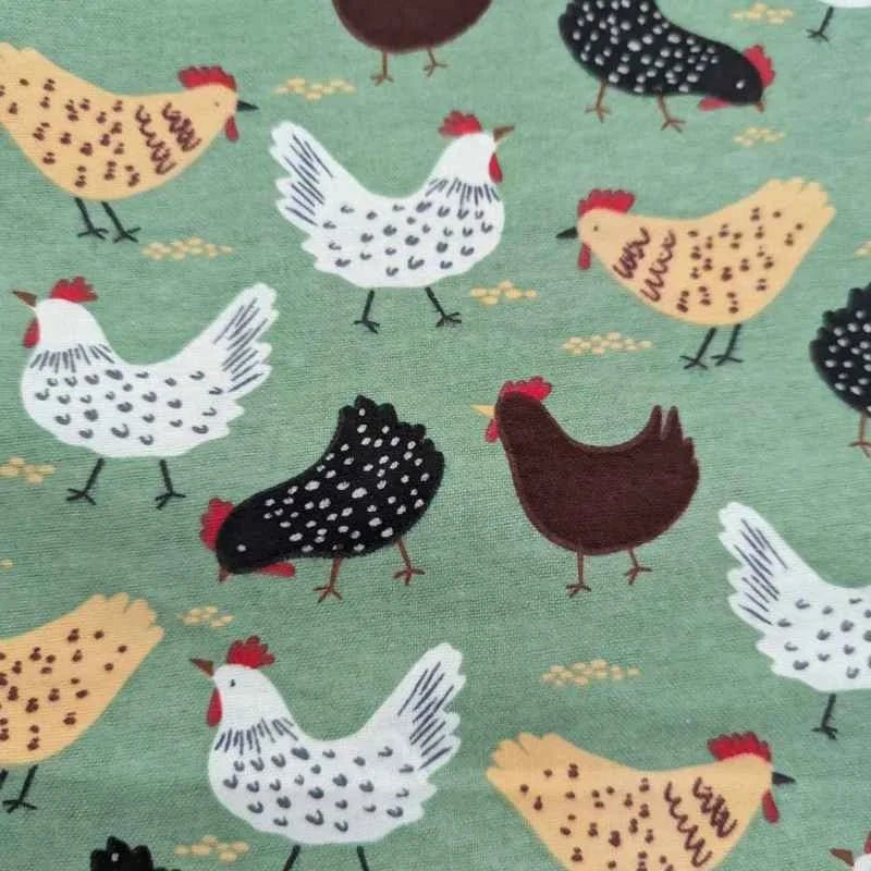 Cotton flannel fabric with beige, black, and white chickens scattered on a soft green background – ideal for quilts, blankets, and farmhouse-themed projects.