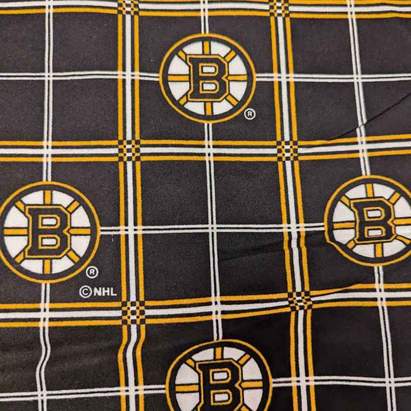 Boston Bruins plaid flannel cotton fabric with black, gold, and white tartan design and repeating NHL Bruins logos.